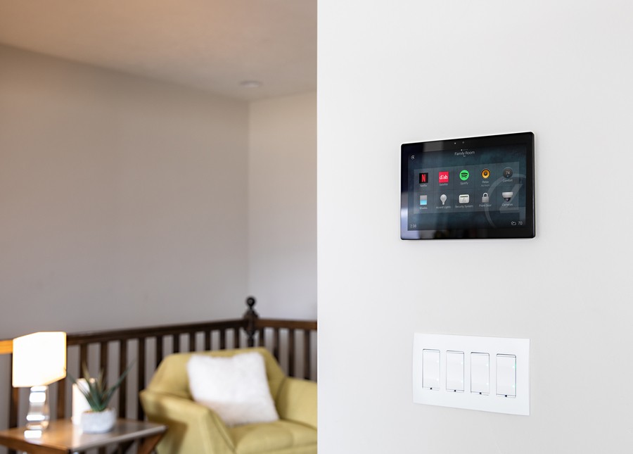 A living space with a tablet mounted on the wall displaying the Control4 interface. 