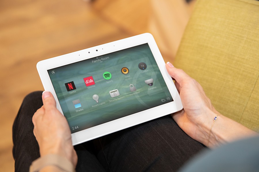 Hand holding a tablet with a Control4 smart home interface on the screen.