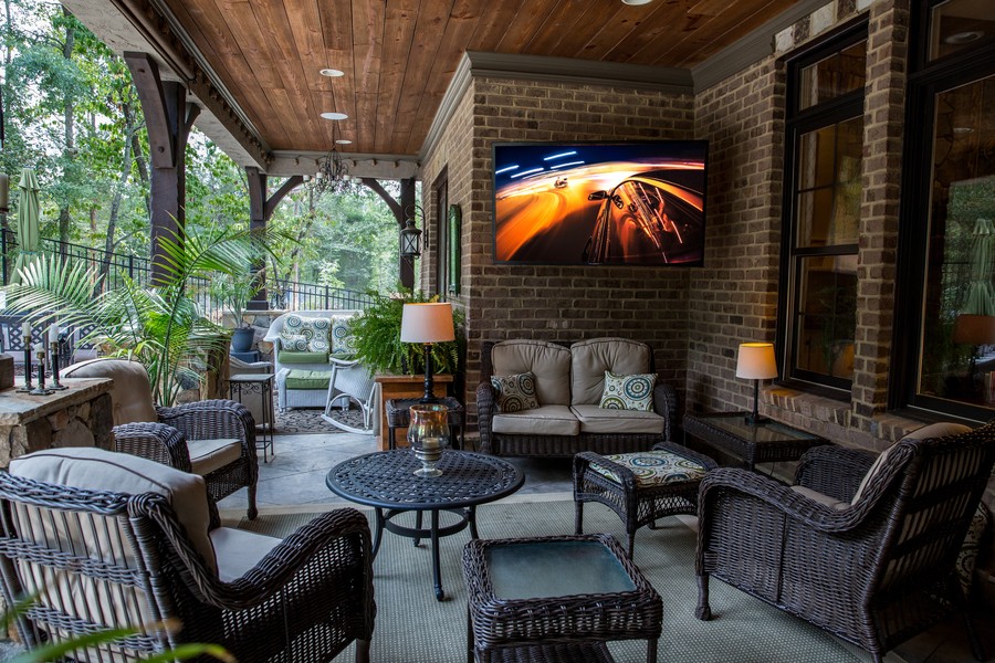 A furnished patio with an outdoor TV mounted on a brick wall. 