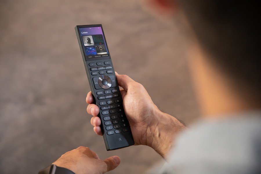 Person’s hand holding a Control4 Halo remote with a Listening screen interface showing