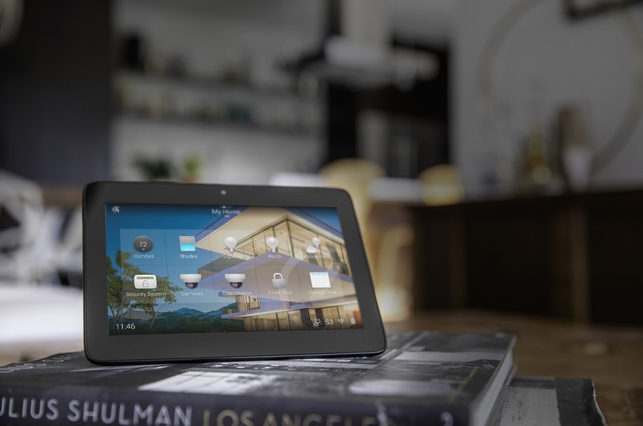 A black tablet perched on a pile of books. On the screen is the Control4 home automation interface. 