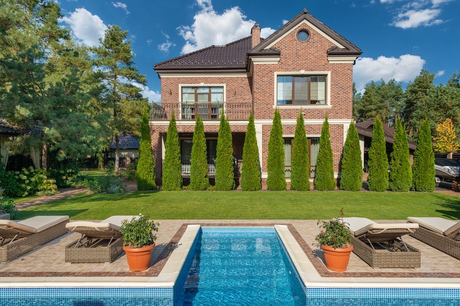 A large brick house with landscaping and a pool in the foreground. 
